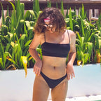 Person wearing a black bikini standing in front of green plants