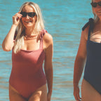Two women in swimsuits standing by a body of water.