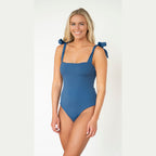 Woman wearing a blue one-piece swimsuit with bow straps on a white background