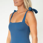Woman wearing a blue sleeveless top with bow straps on a white background