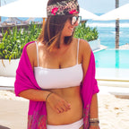 Woman in a white bikini and pink cover-up standing by a pool with ocean view