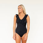 Woman wearing a black one-piece swimsuit with ruffle details on a white background