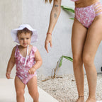 Child and adult wearing matching pink floral swimsuits outdoors.