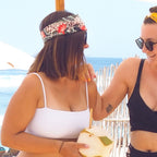 Two women on a beach, one holding a coconut drink, with ocean and sky in the background.