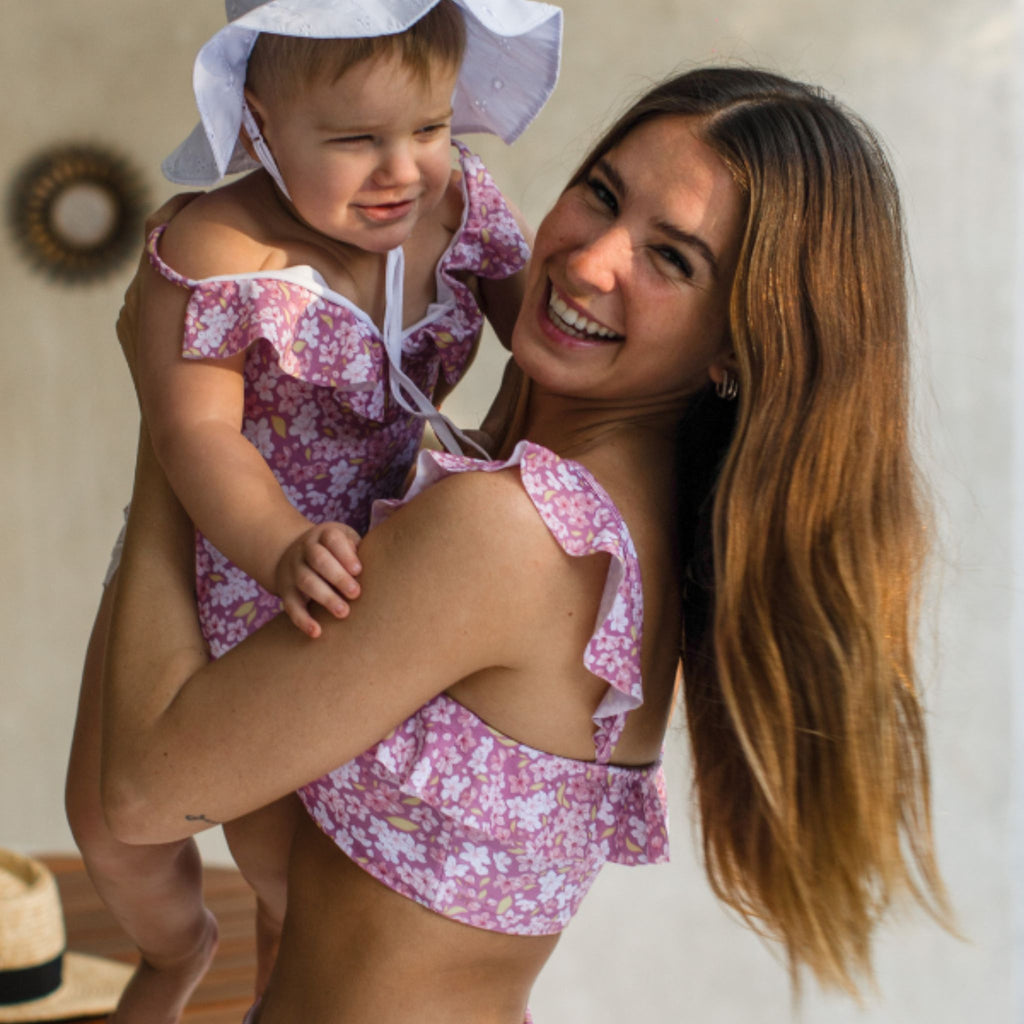 Woman holding a child both wearing matching pink floral outfits indoors.