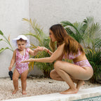 Woman and child in matching pink swimsuits outdoors with plants in the background