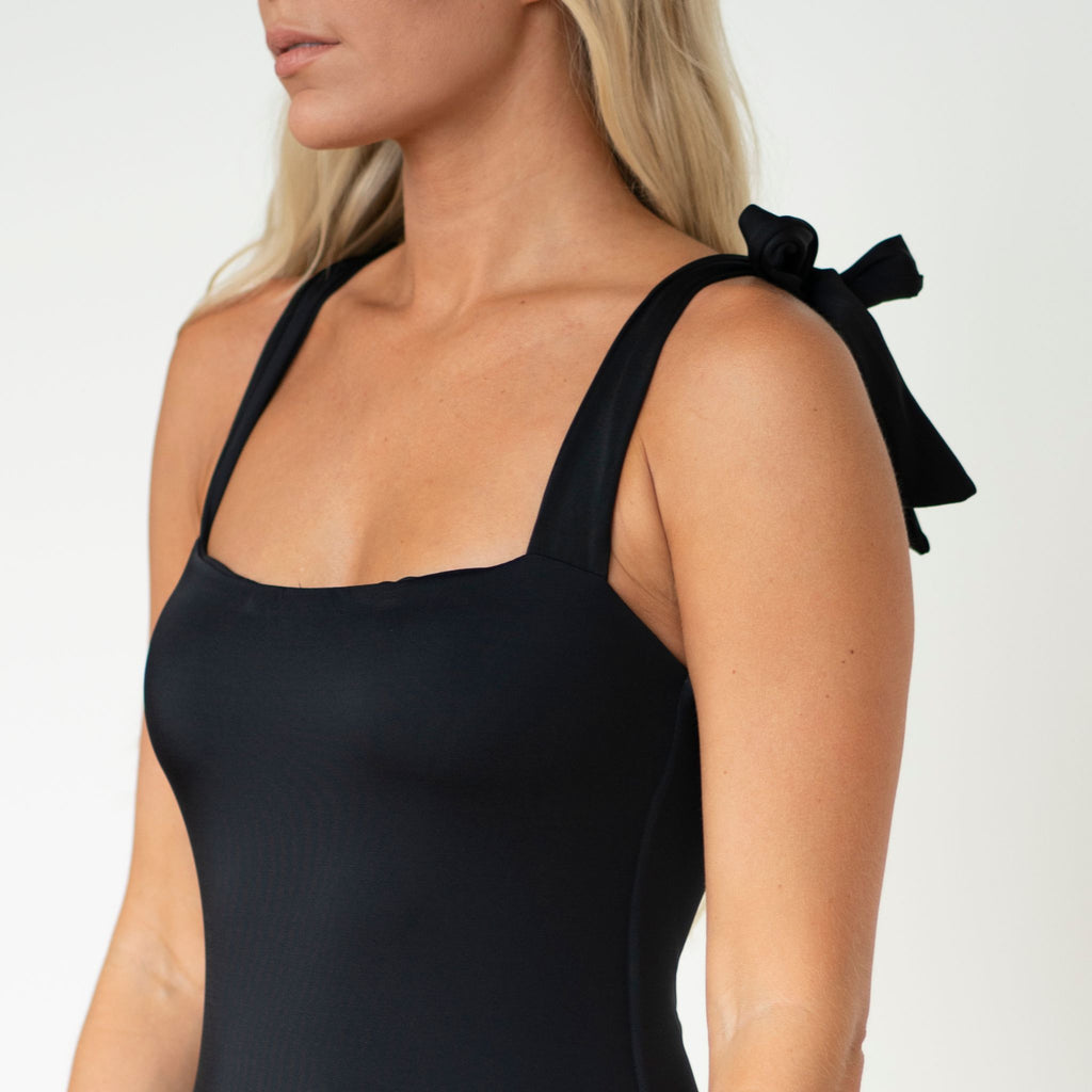 Black sleeveless top with bow details on a plain background