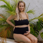 Pregnant Woman wearing a black two-piece outfit sitting outdoors with plants in the background
