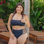 Woman in a black bikini sitting on a wooden bench with green foliage in the background