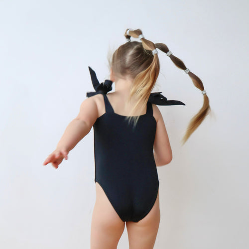 Back view of black kids’ swimsuit with adjustable bowknot straps