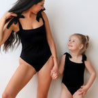 Woman and young girl in matching black swimsuits against a white background